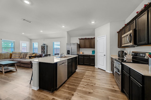 kitchen featuring a kitchen island with sink, stainless steel appliances, lofted ceiling, and light wood-type flooring