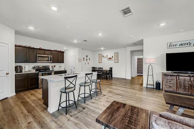 kitchen with a kitchen island with sink, sink, appliances with stainless steel finishes, a kitchen bar, and dark brown cabinetry