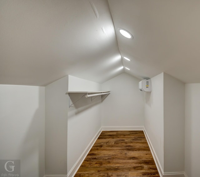 spacious closet featuring lofted ceiling, a wall unit AC, and dark wood-type flooring