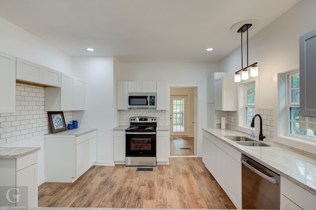 kitchen featuring pendant lighting, white cabinetry, sink, light hardwood / wood-style floors, and stainless steel appliances