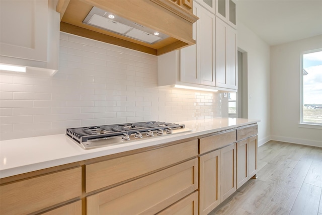 kitchen with backsplash, custom range hood, light hardwood / wood-style flooring, stainless steel gas cooktop, and light brown cabinets