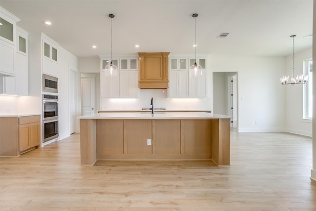 kitchen with hanging light fixtures, a large island with sink, and white cabinetry