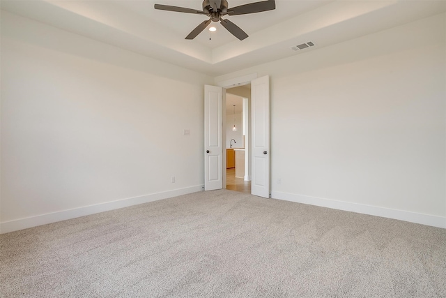 empty room featuring ceiling fan, carpet floors, and a tray ceiling