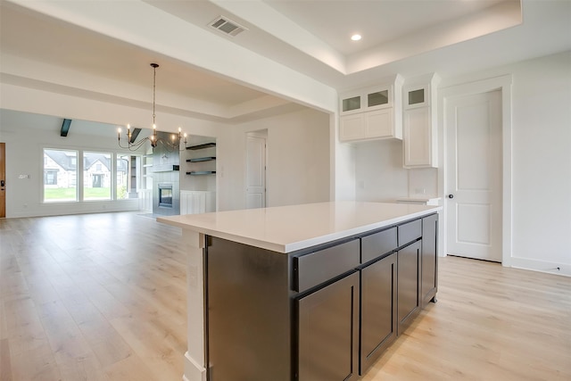 kitchen featuring a center island, light wood-type flooring, a notable chandelier, white cabinetry, and a tray ceiling