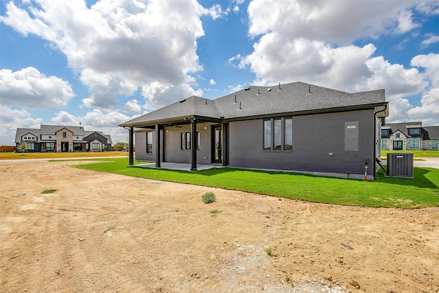 rear view of house with central AC unit and a lawn