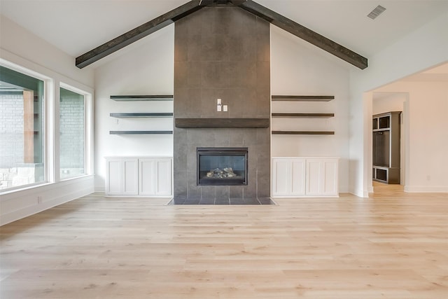 unfurnished living room with a tiled fireplace, high vaulted ceiling, light hardwood / wood-style flooring, and beam ceiling