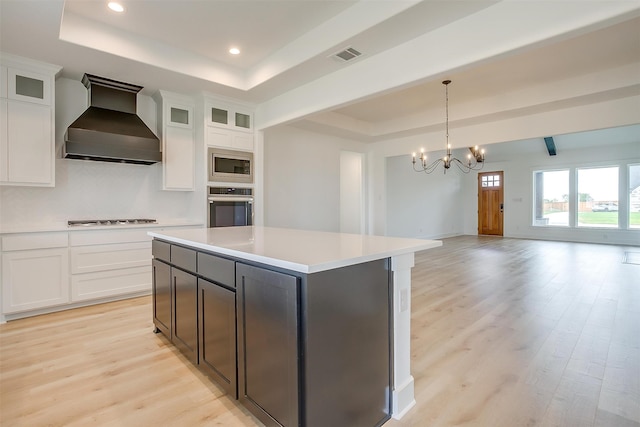 kitchen featuring stainless steel appliances, a kitchen island, an inviting chandelier, a raised ceiling, and custom range hood