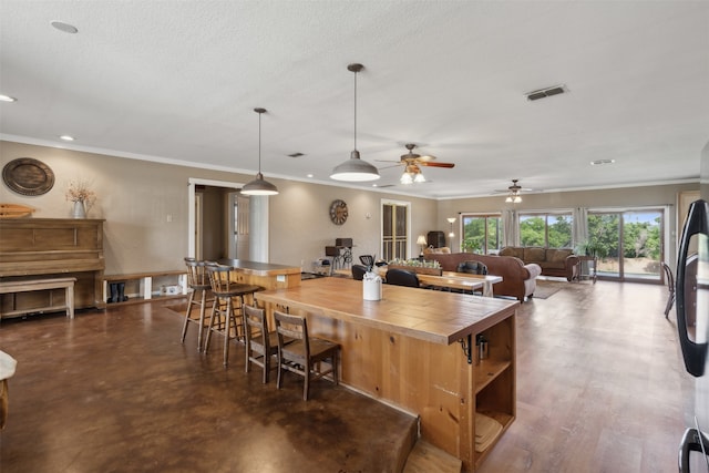 kitchen with ceiling fan, hanging light fixtures, butcher block countertops, a breakfast bar, and ornamental molding