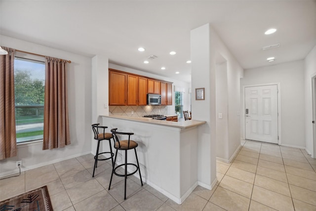 kitchen with backsplash, kitchen peninsula, light tile patterned flooring, and a breakfast bar area