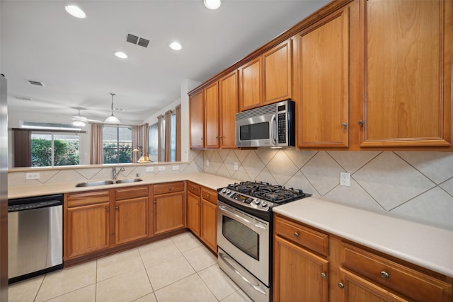 kitchen featuring sink, backsplash, kitchen peninsula, pendant lighting, and appliances with stainless steel finishes