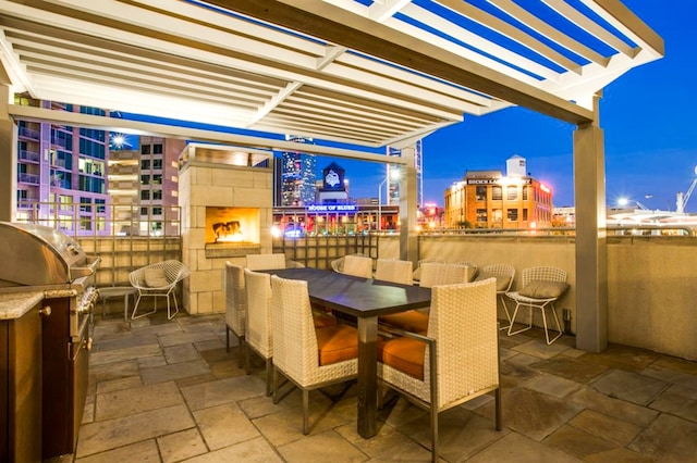 patio terrace at night featuring area for grilling, a pergola, and an outdoor fireplace