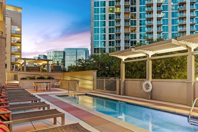 pool at dusk featuring a pergola