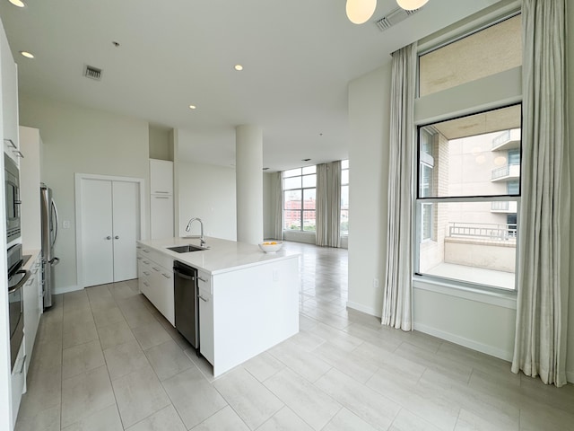 kitchen with stainless steel appliances, white cabinets, a kitchen island with sink, sink, and light tile floors