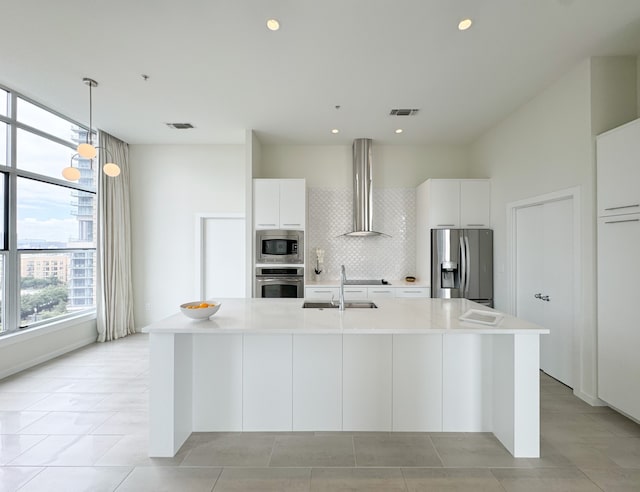 kitchen featuring backsplash, a center island with sink, wall chimney exhaust hood, appliances with stainless steel finishes, and light tile floors