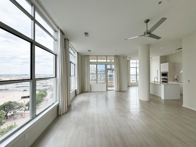 empty room featuring sink, a wealth of natural light, ceiling fan, and a wall of windows