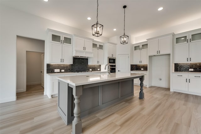 kitchen with stainless steel appliances, pendant lighting, light hardwood / wood-style floors, white cabinetry, and an island with sink