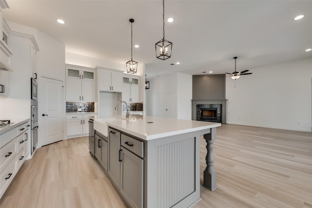 kitchen with ceiling fan, sink, hanging light fixtures, tasteful backsplash, and an island with sink