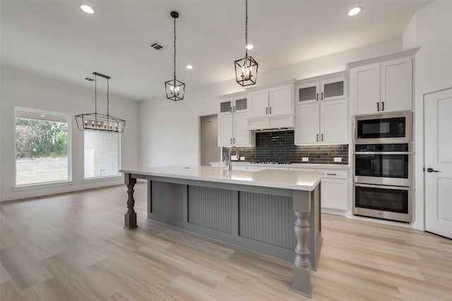 kitchen featuring decorative backsplash, decorative light fixtures, white cabinetry, and a kitchen island with sink