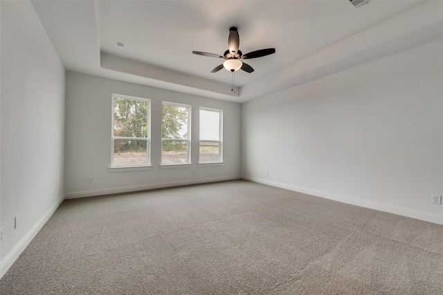 carpeted empty room with a raised ceiling and ceiling fan