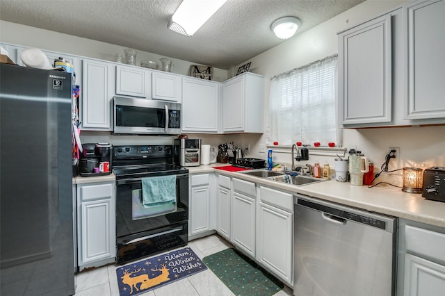 kitchen featuring a textured ceiling, stainless steel appliances, white cabinets, sink, and light tile floors