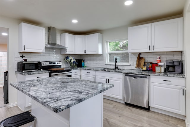 kitchen featuring sink, wall chimney exhaust hood, appliances with stainless steel finishes, tasteful backsplash, and white cabinetry