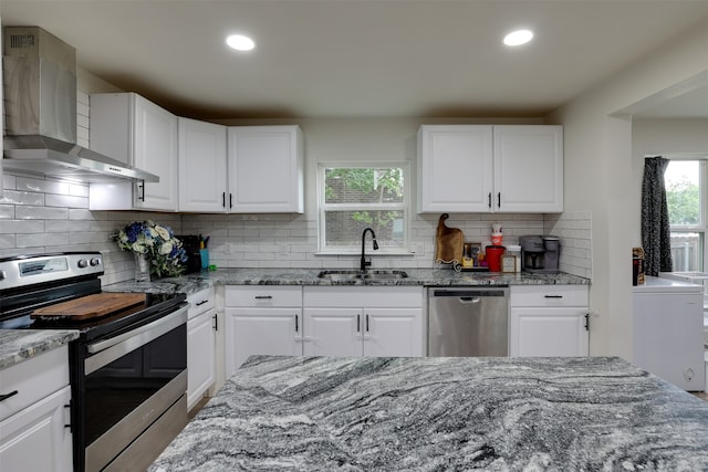 kitchen featuring appliances with stainless steel finishes, light stone counters, wall chimney exhaust hood, sink, and white cabinets