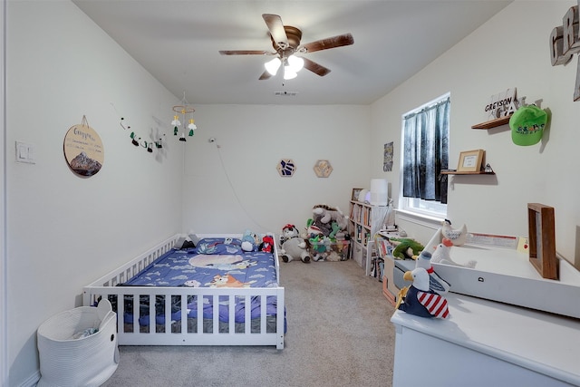 carpeted bedroom with ceiling fan and a nursery area