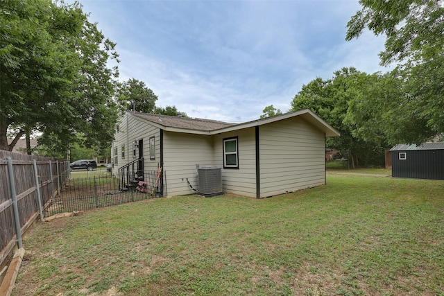 rear view of property featuring central AC, a storage shed, and a lawn