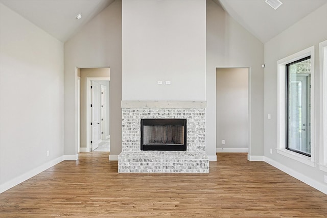 unfurnished living room with a fireplace, high vaulted ceiling, and light wood-type flooring