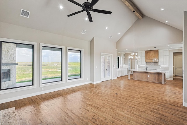 unfurnished living room featuring ceiling fan with notable chandelier, beamed ceiling, high vaulted ceiling, and light wood-type flooring