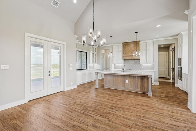 kitchen featuring a large island with sink, french doors, hardwood / wood-style floors, decorative light fixtures, and white cabinets