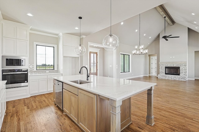 kitchen with white cabinets, a center island with sink, light stone counters, appliances with stainless steel finishes, and sink