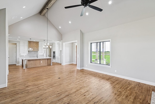 unfurnished living room featuring beam ceiling, high vaulted ceiling, light hardwood / wood-style flooring, and ceiling fan with notable chandelier