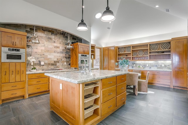 kitchen featuring light stone counters, high vaulted ceiling, a center island with sink, pendant lighting, and decorative backsplash