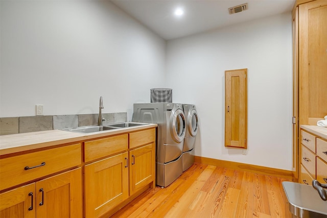 washroom with separate washer and dryer, sink, cabinets, and light wood-type flooring