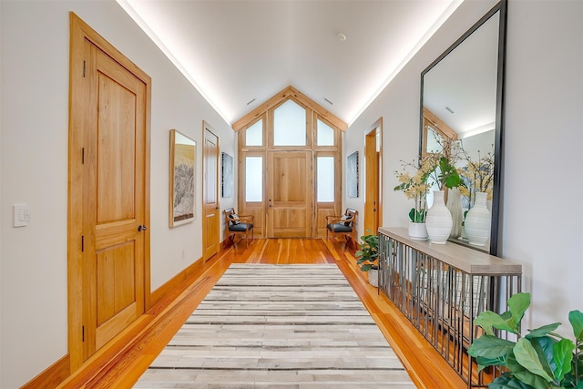 corridor with ornamental molding, vaulted ceiling, and light wood-type flooring