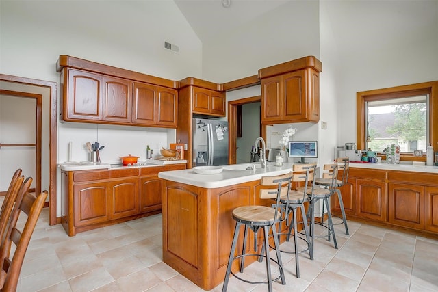 kitchen featuring a center island with sink, stainless steel fridge, high vaulted ceiling, and a kitchen bar