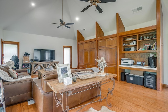 living room with ceiling fan, high vaulted ceiling, built in desk, and light hardwood / wood-style floors