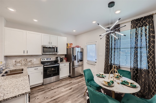 kitchen featuring light hardwood / wood-style floors, hanging light fixtures, white cabinetry, stainless steel appliances, and tasteful backsplash