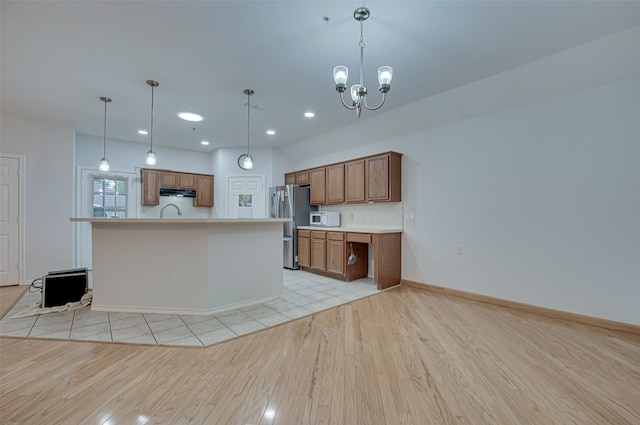 kitchen featuring a center island with sink, stainless steel fridge, light tile flooring, and pendant lighting