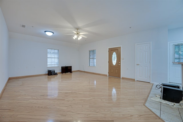 unfurnished living room featuring light hardwood / wood-style floors, a wood stove, and ceiling fan