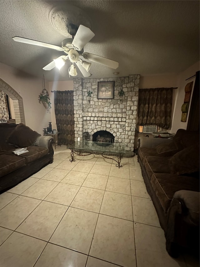 tiled living room with ceiling fan, a textured ceiling, brick wall, and a brick fireplace