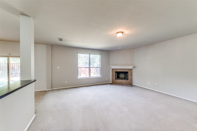 unfurnished living room featuring light carpet, a textured ceiling, and a tile fireplace