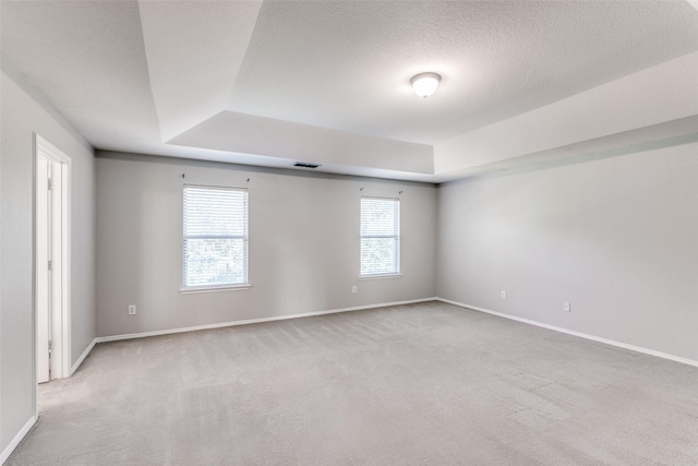 unfurnished room with a tray ceiling, a textured ceiling, visible vents, carpet floors, and baseboards