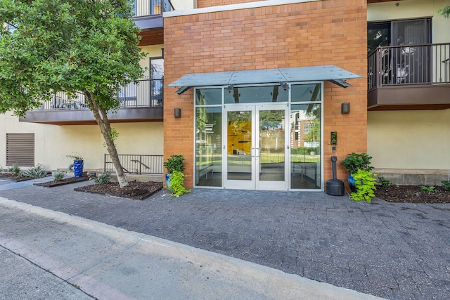 entrance to property with stucco siding, brick siding, a balcony, and french doors