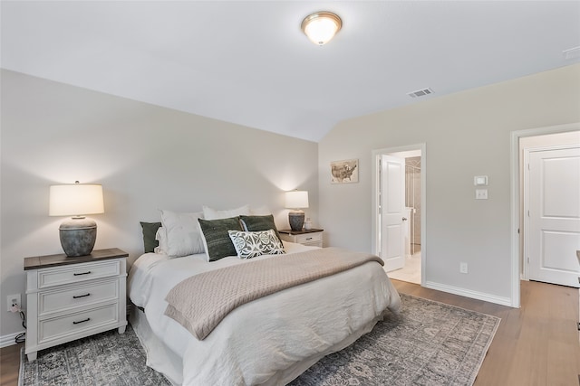 bedroom featuring ensuite bathroom, vaulted ceiling, and hardwood / wood-style flooring