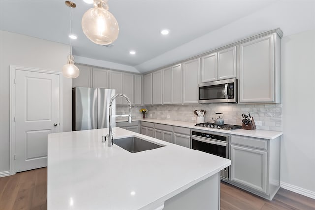 kitchen featuring hanging light fixtures, sink, stainless steel appliances, and a kitchen island with sink