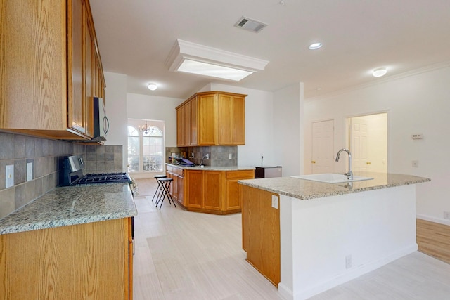 kitchen featuring gas stove, an island with sink, tasteful backsplash, sink, and light wood-type flooring