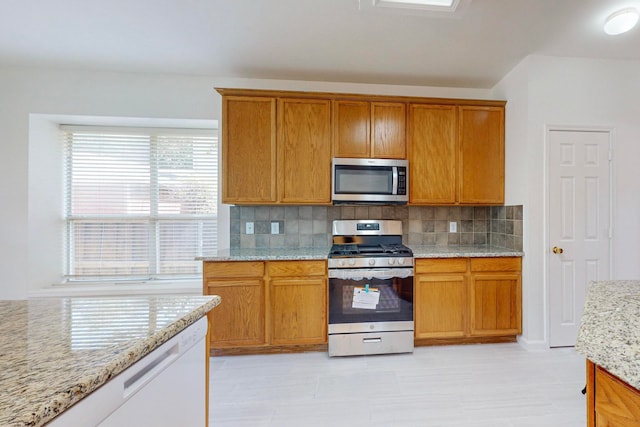 kitchen featuring appliances with stainless steel finishes, light tile patterned floors, decorative backsplash, and light stone countertops