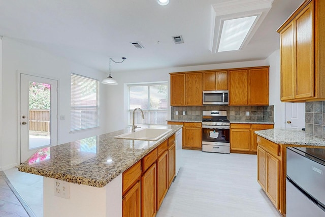 kitchen with decorative backsplash, appliances with stainless steel finishes, a center island with sink, light tile patterned floors, and sink